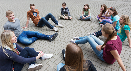 Eine Gruppe junger Menschen sitzt im Kreis auf einer gepflasterten Flche.